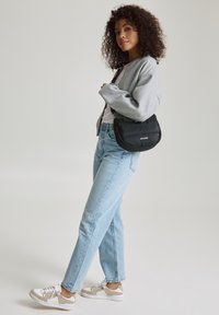 Sac à main noir matelassé de forme incurvée, associé à un sweatshirt gris surdimensionné, un t-shirt blanc, un jean droit bleu clair et des baskets beiges.