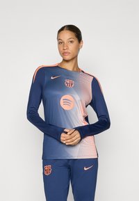 Haut de sport à manches longues en bleu marine avec des accents orange. Présente un design dégradé, le logo de Barcelone, et une marque Spotify sur le devant.