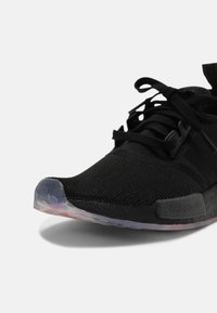 Black athletic shoe with a textured knit upper, lace-up closure, and a semi-transparent rubber sole featuring a hexagonal pattern.