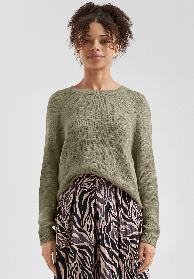 Olivengrüner Strickpullover mit lockerer Passform und gerippten Bündchen, kombiniert mit einem Faltenrock im Schwarz-Pink-Zebra-Muster.