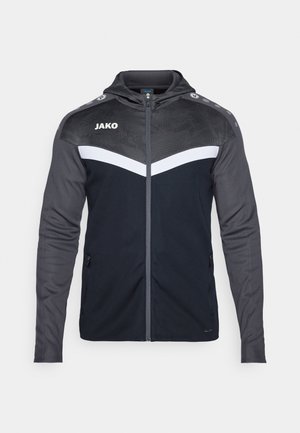 Zwarte en grijze sportjack met een rits aan de voorkant, capuchon en een witte strook over de borst. Heeft een gestructureerd bovenpaneel en zijzakken.