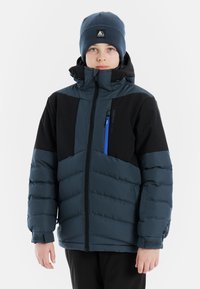 Gesteppten marineblauem Jacke mit schwarzen Akzenten, Frontreißverschluss und blauer Tasche. Getragen mit einer passenden Strickmütze. Texturierte Ärmel mit Bündchendetail.