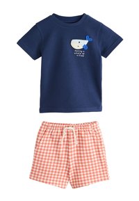 Chemise bleu marine à manches courtes avec un motif de baleine et le texte « Having a whale of a time », associée à un short à carreaux rose et blanc avec cordon de serrage.