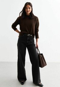 Mörkbrun stickad tröja, höga svarta vida jeans, svarta pumps med spetsig tå, håller en brun strukturerad handväska.