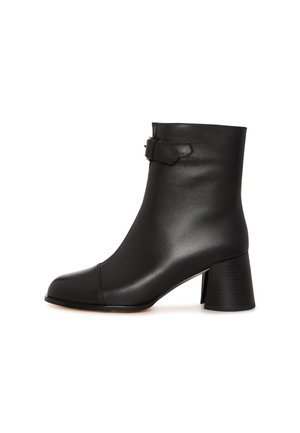 Schwarze Leder-Ankle-Boots mit glatter Textur, spitzem Schuhkopf und blockförmigem Absatz. Mit einem dekorativen Riemen-Detail an der Seite.