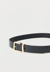 Μαύρη δερμάτινη ζώνη με χρυσή ορθογώνια αγκράφα και θηλιά, απλωμένη επίπεδη με το άκρο περασμένο μέσα από τη θηλιά σε απλό λευκό φόντο.