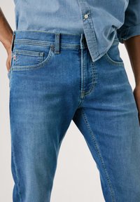 Jeans in denim azzurro chiaro con taglio dritto, caratterizzati da cuciture gialle, un piccolo etichetta logo sulla tasca e un classico design a cinque tasche.