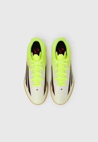 Ζεύγος αθλητικών παπουτσιών σε νέον κίτρινο και λευκό με μαύρες και κόκκινες λεπτομέρειες, απει κονισμένα από πάνω σε λευκό φόντο.