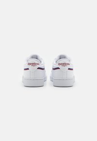 Sapatilhas veganas brancas da Reebok com uma textura suave, apresentando um logótipo vermelho e detalhes azuis na lateral, bico redondo e sola de borracha.