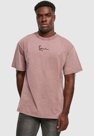 Light pink cotton short-sleeve t-shirt with a crew neck and subtle black embroidered logo on the chest. Fabric appears slightly textured.