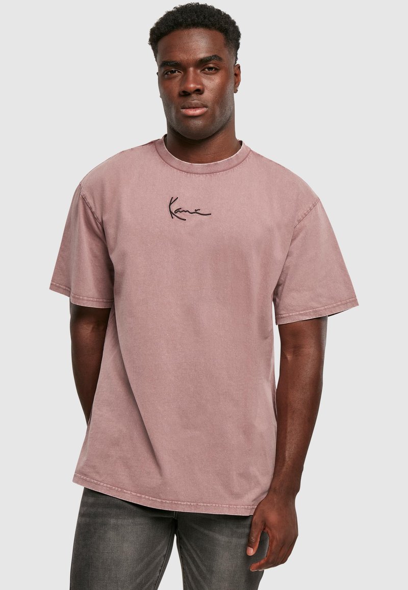 Heledast roosa puuvillane lühikeste varrukatega T-särk ümmarguse kaelusega ja õrn must tikand rinnal. Kangas näib olema veidi struktureeritud.