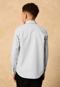 Lichtblauw overhemd met lange mouwen, een button-down kraag en een afgeronde zoom, voorzien van een gladde textuur en manchetten met knopen.