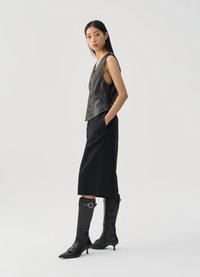 Black leather sleeveless top with a V-neck, paired with high-waisted black trousers and knee-high black boots with pointed toes.
