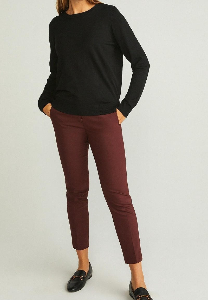 Pull noir à manches longues avec un col rond, associé à un pantalon bordeaux ajusté. Des mocassins noirs complètent la tenue, présentant une texture lisse.