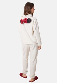 Hvid fleece hoodie med en stor rød og mørk sløjfe på ryggen, parret med matchende hvide fleece bukser og burgunder bløde slippers.