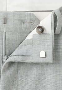 Ceinture de pantalon en tissu gris clair texturé montrant une fermeture éclair, un bouton, une fermeture crochet-et-barre, et une doublure intérieure blanche.