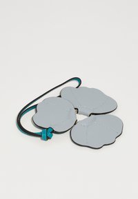 Grå lærblomstformet tilbehør med sorte kanter. Har tre kronblade forbundet med et blåt bånd, kantet med diskret syning.