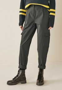 Zwarte cargobroek met een relaxte pasvorm, voorplooien, zijzakken en opgerolde mouwen, gecombineerd met zwarte veterschoenen in militaire stijl.