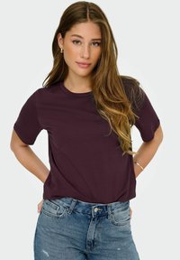 T-shirt a maniche corte color bordeaux, col rotondo, in cotone, vestibilità comoda, abbinato a jeans chiari e strappati, con bracciale dorato in evidenza.