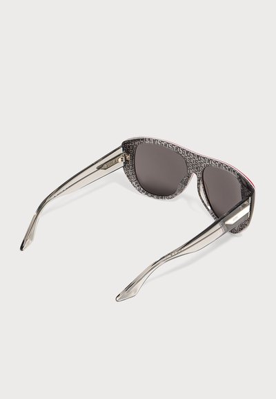 Γυαλιά ηλίου με σκουρόχρωα φακούς και διαφανή σκελετό, με σχέδιο στο πλαίσιο που επαναλαμβάνει γράμματα και μεταλλικές λεπτομέρειες στα πλαϊνά.