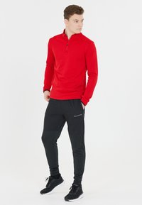 Rode ritslongsleeve top gecombineerd met zwarte sportbroek met zijzakken en een gestructureerde afwerking. Zwarte sneakers maken de outfit compleet.