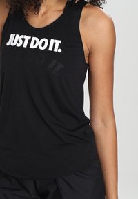 Débardeur de sport noir avec un col rond et une coupe dos nageur. Présente un texte blanc audacieux "JUST DO IT." à l'avant. Texture de tissu doux.