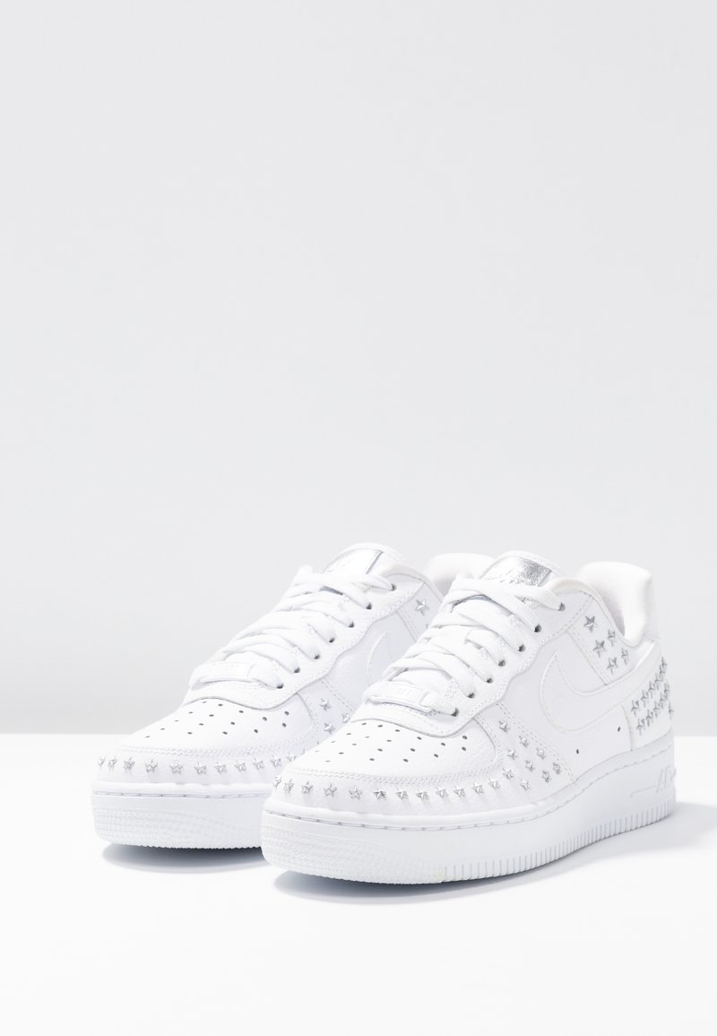 Weiße Nike Air Force 1 Sneakers mit perforierter Zehenpartie, glattem Leder, sternförmigen Nieten an den Seiten und strukturiertem Gummisohle.