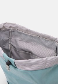 Helleblaue Stofftasche mit offenem Oberteil, die das grau-weiße gestreifte Innenfutter und eine Innentasche zeigt.