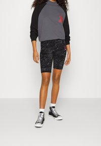 Svart och grå atletisk outfit bestående av en kortärmad topp med röda detaljer och texturerade svarta cykelshorts, kombinerad med svarta högskor.