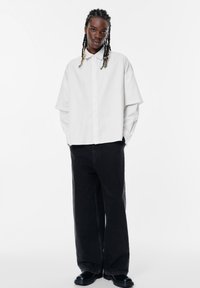 Wit gestreepte oversized button-up shirt met een kraag en brede mouwen, gecombineerd met zwarte brede jeans en zwarte schoenen. Eenvoudig ontwerp.