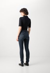 Černý top s krátkým rukávem, kombinovaný s tmavě modrými, těsně padnoucími džíny. Džíny mají klasický pětikusový design a koženou nášivku na zadní straně.