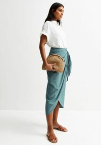 Lightweight, teal wrap skirt with a textured pattern, paired with a white button-up shirt and brown slide sandals. Holds a woven clutch.