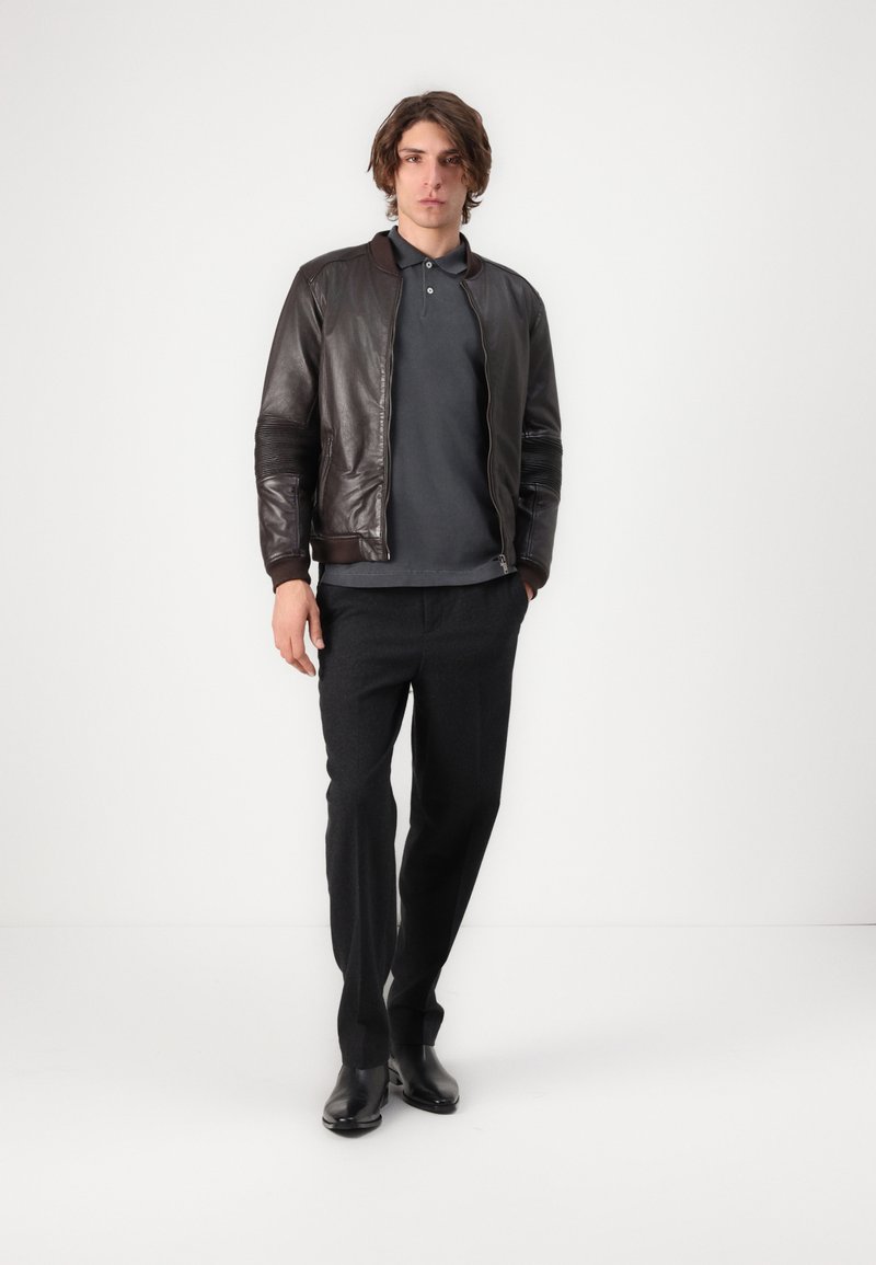 Bruine leren bomberjack met geribbelde manchetten, grijze poloshirt, antraciet pantalon en zwarte dress boots. Minimalistisch ontwerp op een effen achtergrond.