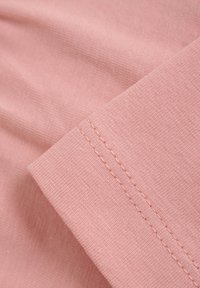 Ljust rosa tyg med en subtil textur, som visar en närbild av en vikt kant och synlig sömnad. Slät och mjuk yta.