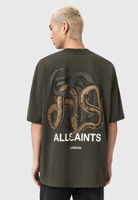 Oliwkowa bawełniana koszulka z dużą grafiką węża w czerni i złocie na plecach, z nadrukiem "ALLSAINTS" i "LONDON" poniżej.