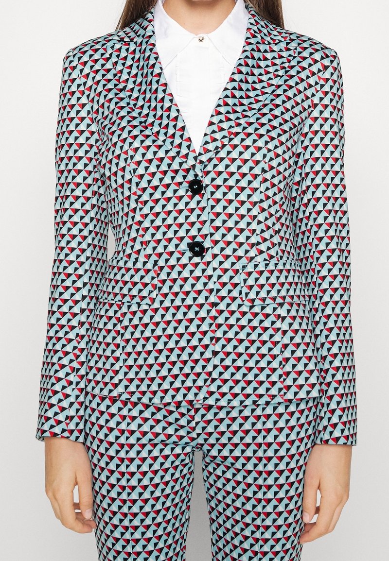 Un costume à motifs composé d'un tissu avec un design géométrique de triangles bleus, rouges et noirs ; il comporte deux boutons et des poches.
