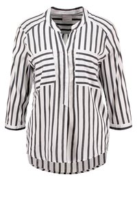 Blouse blanche à manches longues avec des rayures noires verticales, deux poches poitrine avant avec des rayures horizontales et un col mandarin.