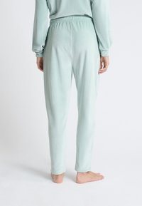 Pantalons de pyjama côtelés vert clair avec une taille élastique et des jambes fuselées, présentant une texture douce et une coupe décontractée.