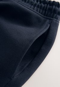 Nahaufnahme von marineblauem, geripptem Stoff mit einem elastischen Bund und einer seitlichen Taschenöffnung an der Kleidung.