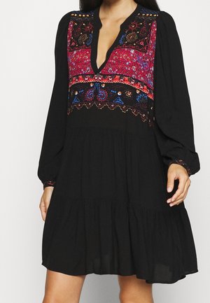 Czarna sukienka z długim rękawem, głębokim dekoltem w kształcie litery V oraz kolorowym haftem kwiatowym w odcieniach czerwieni, niebieskiego i pomarańczowego na wysokości klatki piersiowej i mankietów.