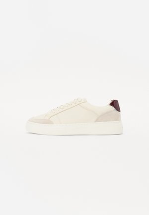 Sneakers z kremową skórzaną cholewką, z beżowymi zamszowymi akcentami, bordowym tabem na pięcie i grubą białą gumową podeszwą. Z zapięciem na sznurowadła.