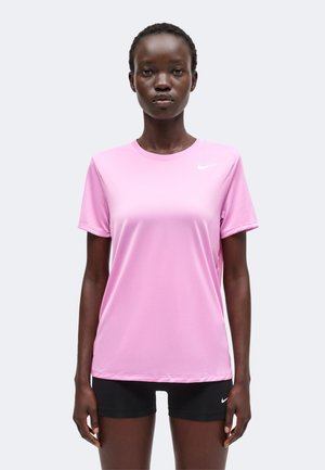 Femme debout face à l'avant portant un t-shirt rose clair à manches courtes et un short noir avec de petits logos Nike blancs sur les deux.