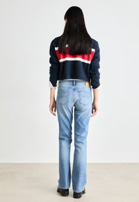 Cropped navy sweater with red and white stripes, paired with light blue flared jeans. Features a tapered fit and classic five-pocket design.