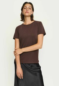 T-shirt marrone a maniche corte in tessuto morbido con scollo rotondo, abbinato a una gonna nera in satin, presentato su uno sfondo neutro.