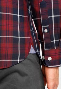 Rode en marineblauwe geruite overhemden met witte accenten, met een visgraatstructuur en een ronde zoom. Knopen op de manchetten.