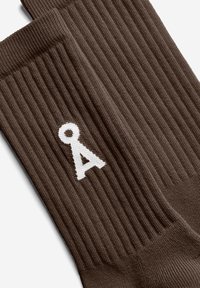 Bruine geribde sokken met een witte letter "A" als ontwerp. De textuur is glad en zacht, met een reguliere sokvorm.