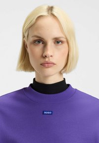 Paarse sweatshirt met een geribbelde kraag, voorzien van een blauw "HUGO"-logo op de borst. Soepele stofstructuur, slim fit ontwerp.
