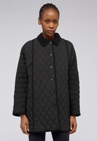 Svart vadderad jacka med krage, med en framknäppning, kontrasterande pipings och ett diamantmönster genom hela plagget.