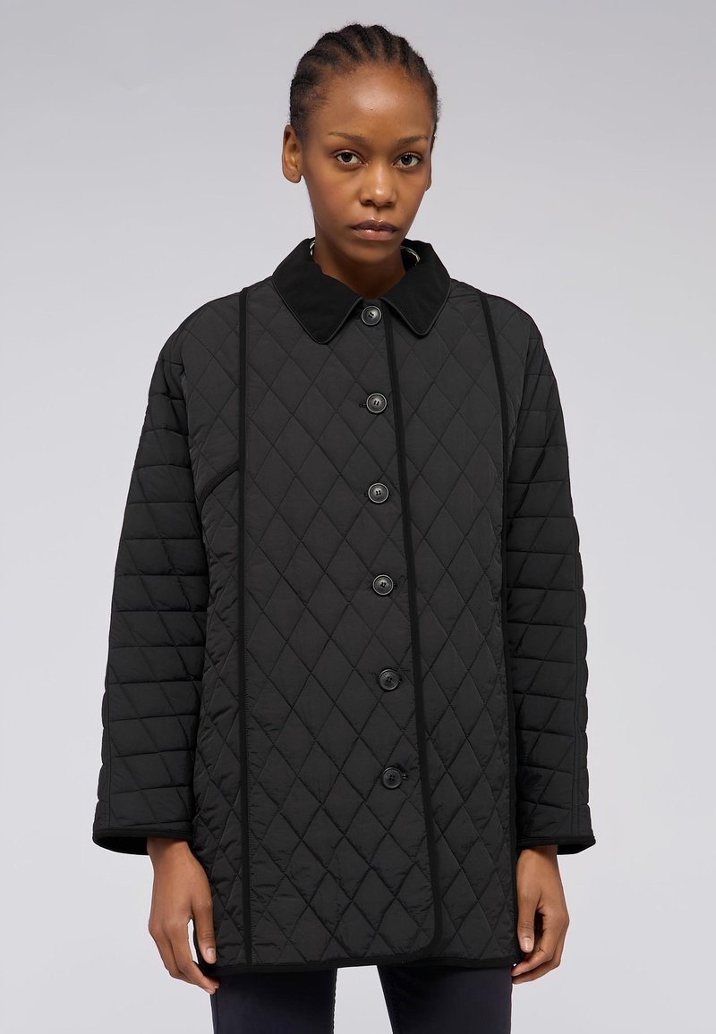 Svart vadderad jacka med krage, med en framknäppning, kontrasterande pipings och ett diamantmönster genom hela plagget.