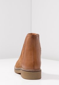 Botte de cheville en cuir marron avec des accents en daim texturé, bord ondulé et semelle en caoutchouc basse. L'arrière présente une finition lisse.
